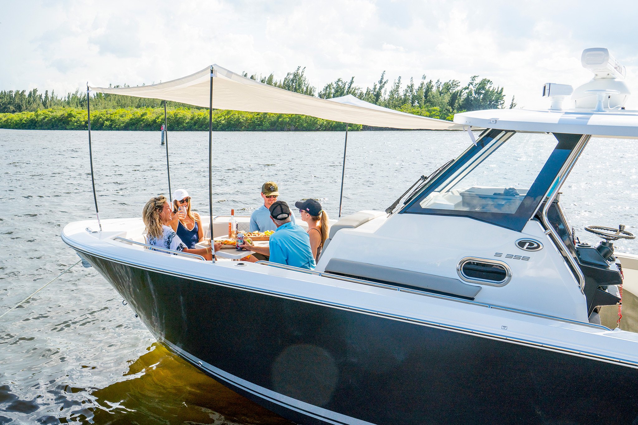 A group of happy boaters dine under the sunshade on the bow of Pursuit Boats S 358 Sport boat.